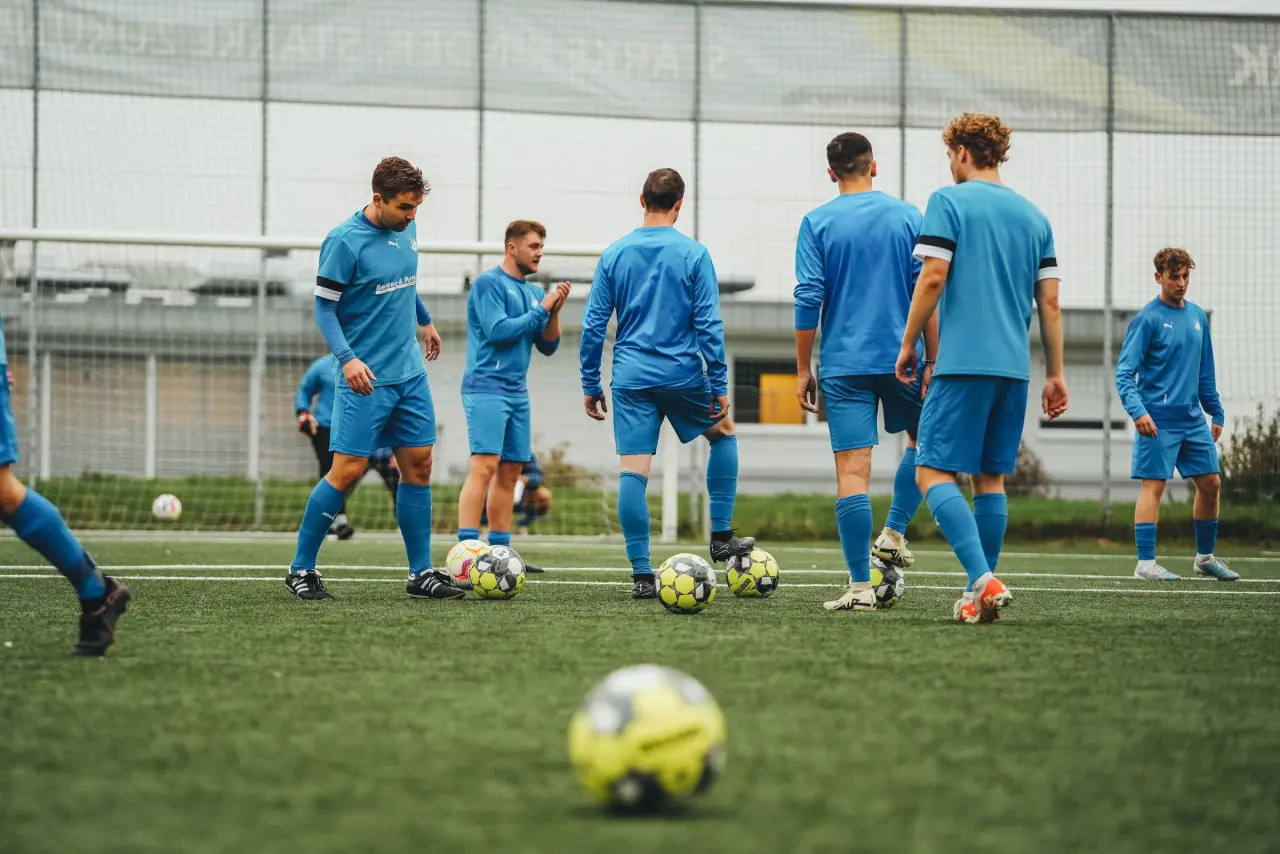 Soccer players in blue training tops work through a drill on an artificial pitch.